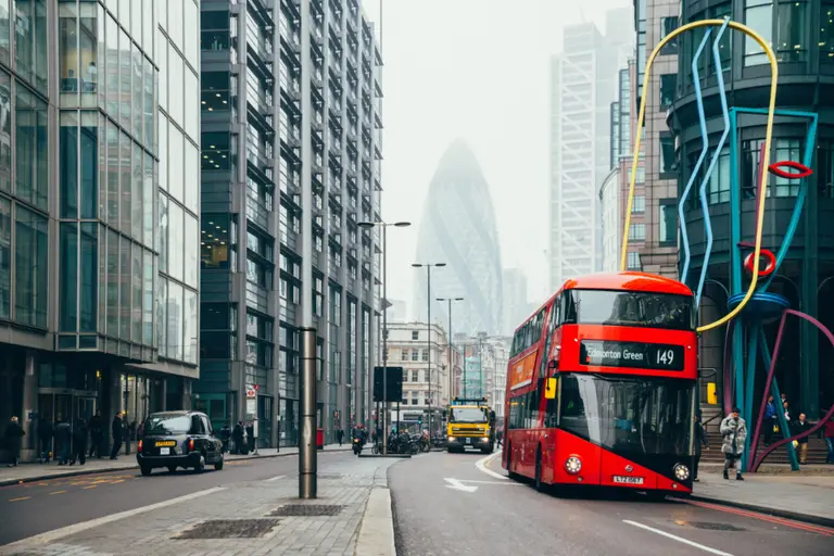 Red London double-decker bus on a city street near the Gherkin